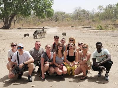 A group of guests on safari with zebras and wildlife behind them.